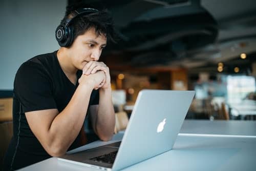 man-wearing-headphones-while-sitting-on-chair-in-front-of-MacBook